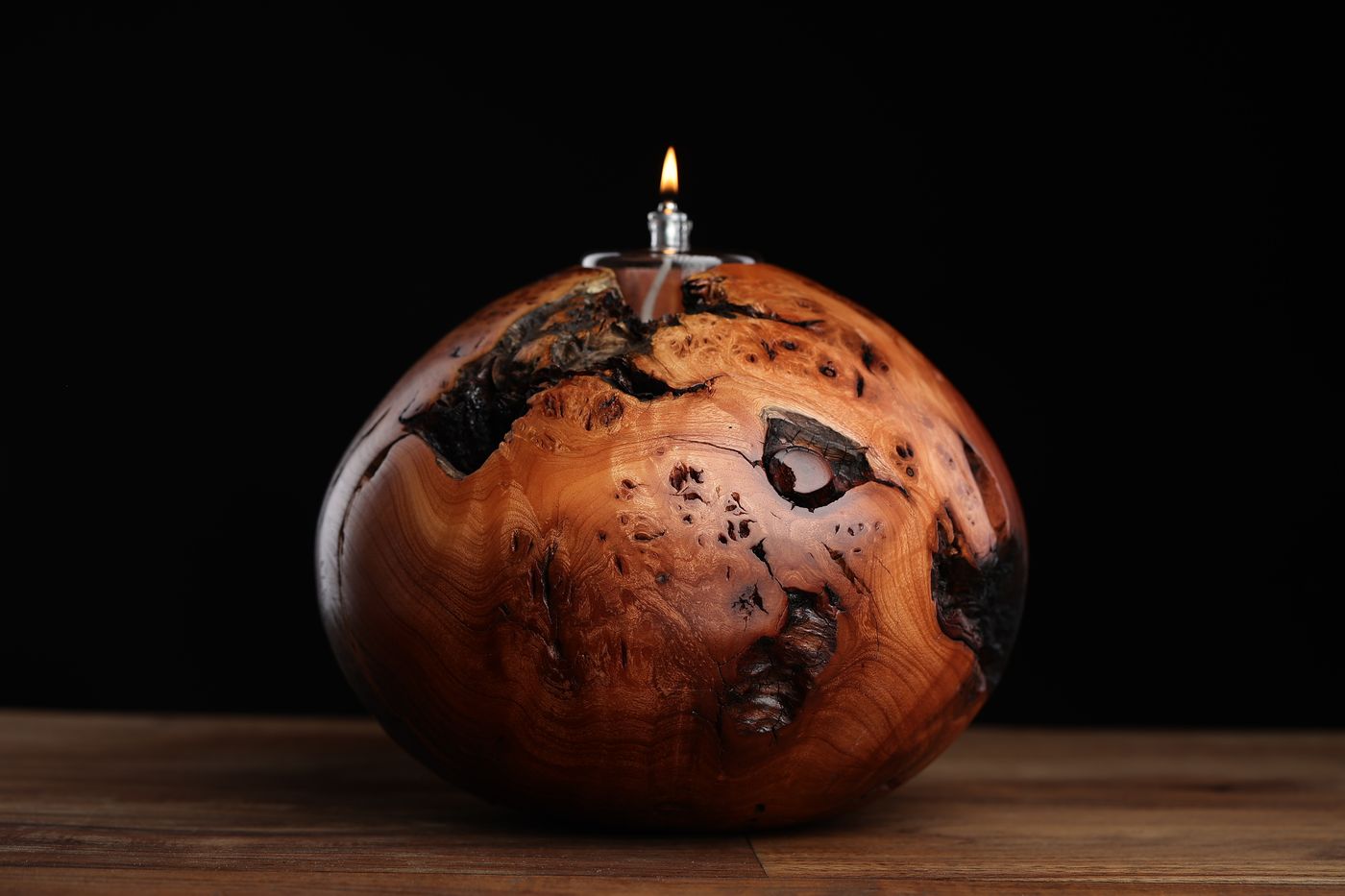 Escalante: a large spherical juniper burl oil lamp with charred continents across polished amber, lit