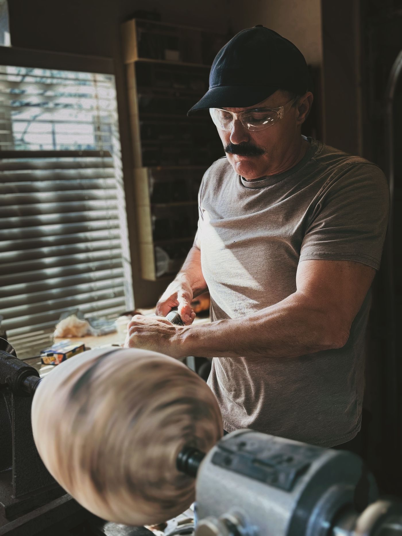 The maker at the lathe, turning a spinning juniper burl by hand in a sunlit workshop